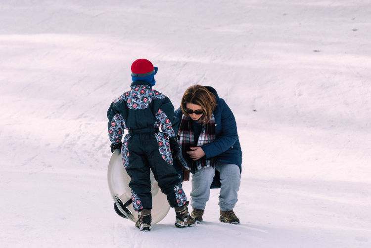 Full length of boy tobogganing by mother on snow