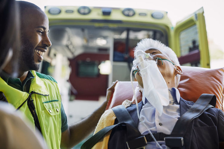 Smiling male paramedic encouraging businessman against ambulance