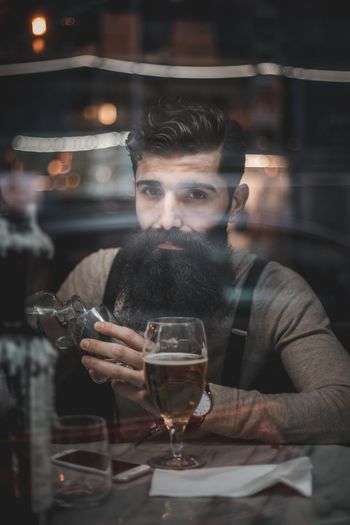 Portrait of man seen through glass window holding glass while sitting in restaurant