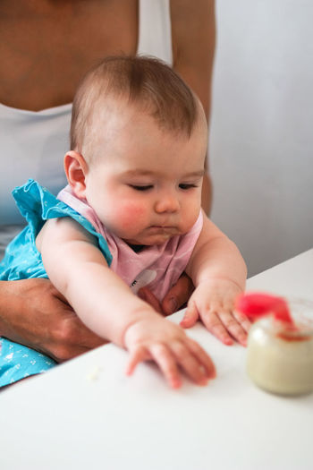 Child at a table with jar with vegetable puree and spoon. baby girl tries to eat herself.
