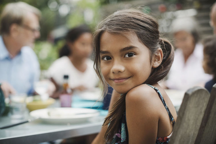 Portrait of smiling girl sitting with family at outdoor dining table