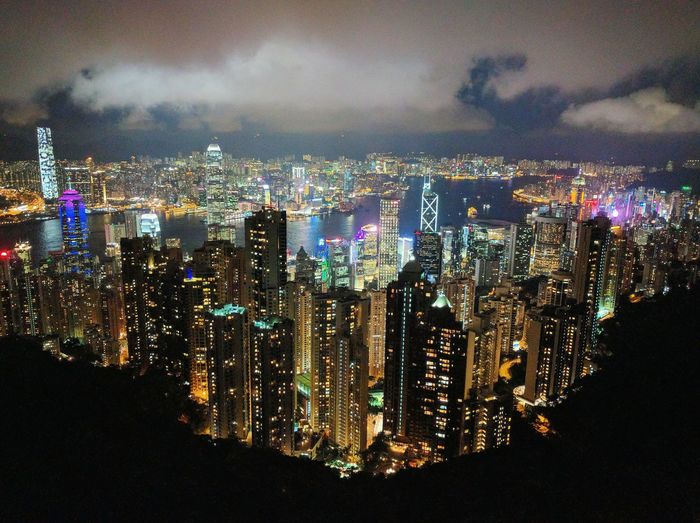 Aerial view of illuminated buildings against cloudy sky in city seen through victoria peak