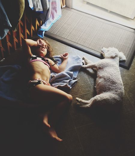 High angle view of girl in bikini lying down by dog on floor