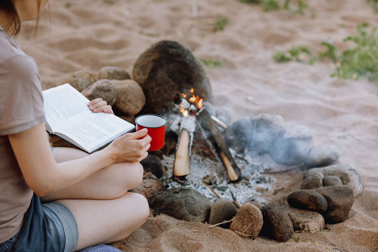 Woman's hand holds a red cup over a campfire in nature. campfire on a hike in the forest. traveling