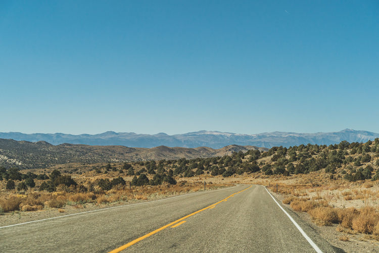 Empty road along landscape against clear blue sky