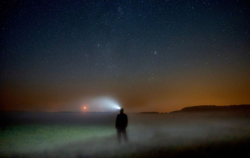 Silhouette person standing on field against sky at night