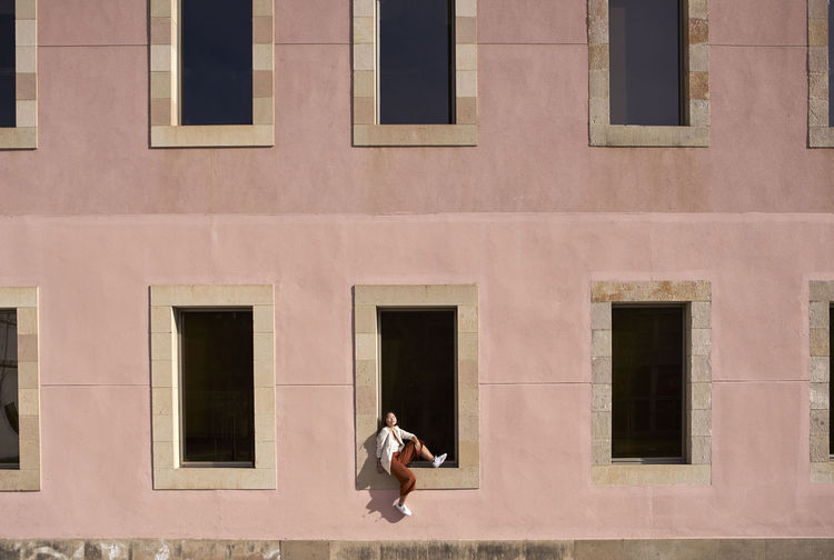 Woman sitting on window sill of building during sunny day