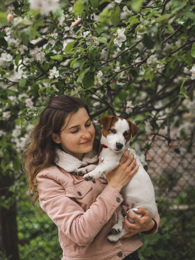 Beautiful woman with dog standing against tree outdoors