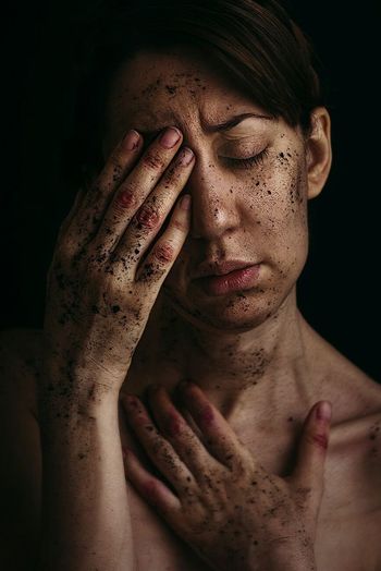 Close-up of topless young woman with dirt against black background