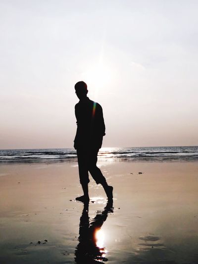 Silhouette man walking at beach against sky