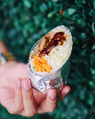 Cropped image of hand holding food covered in foil