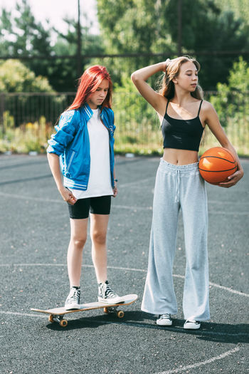 Portrait of two teenage girls with a basketball and a skateboard on a sports field