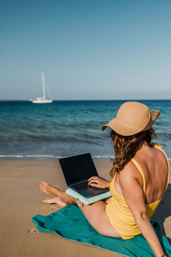 Woman using laptop at beach against clear sky