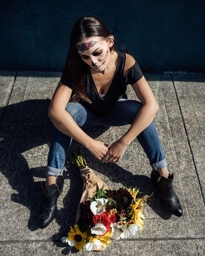 Woman with spooky halloween make-up sitting by bouquet on footpath