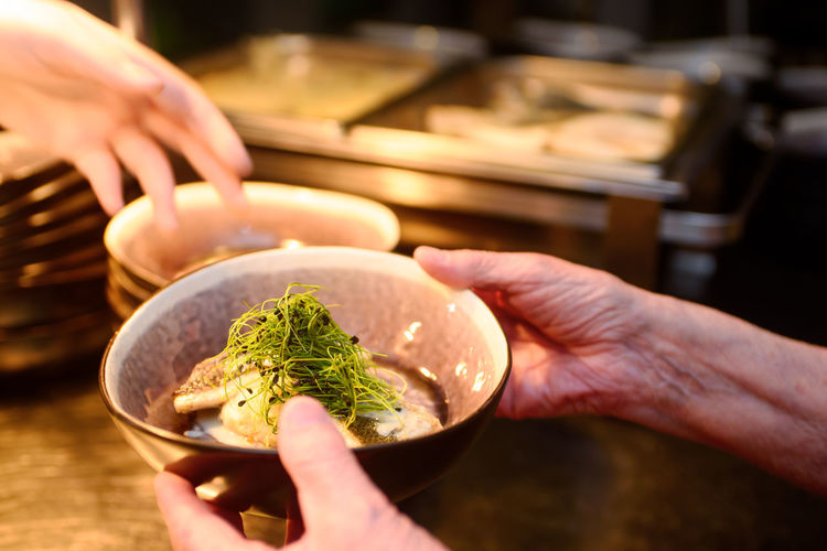 Hand with a bowl containg fish and fresh cuckooflower and blurred buffet in the background