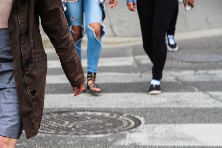 Midsection of woman walking on zebra crossing with people in background