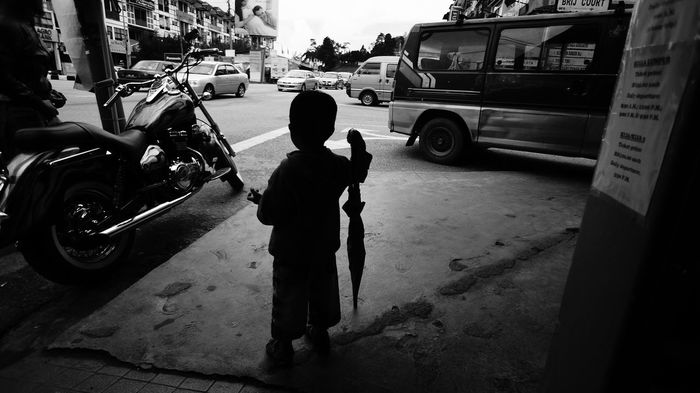 Rear view of boy standing with umbrella on street