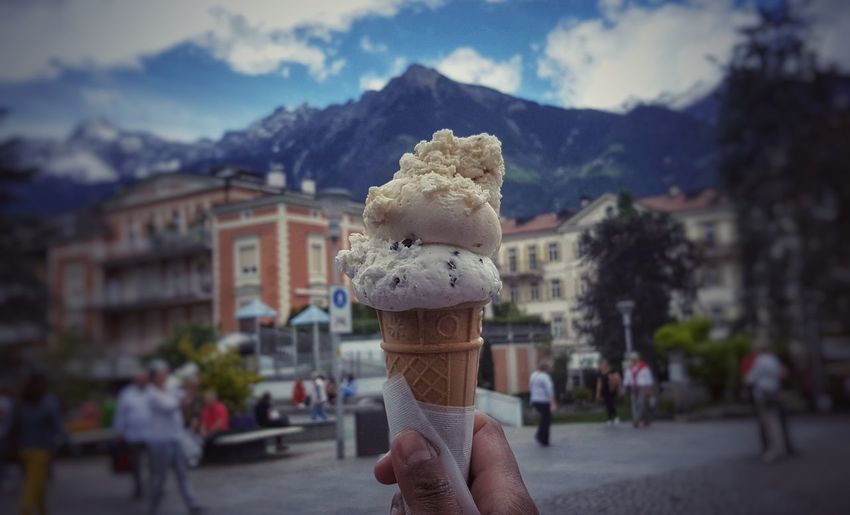 Cropped hand holding ice cream against mountain in town