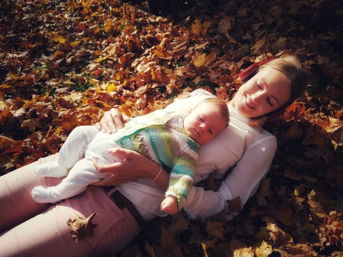 High angle view of mother with son lying on dry leaves during autumn