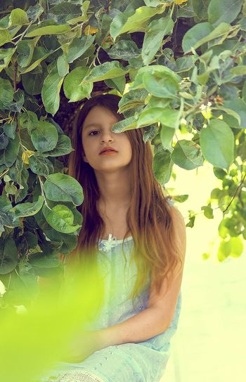 Portrait of young woman standing against tree
