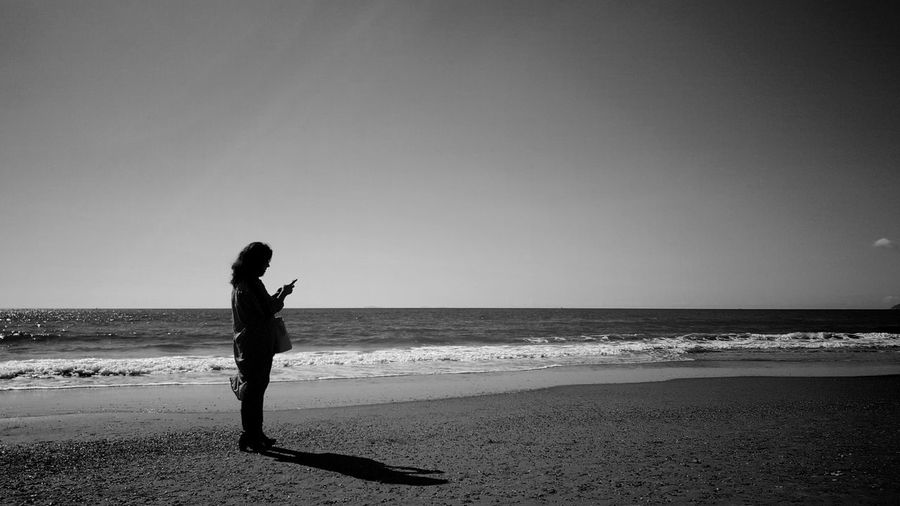 Full length of woman using phone at beach against sky