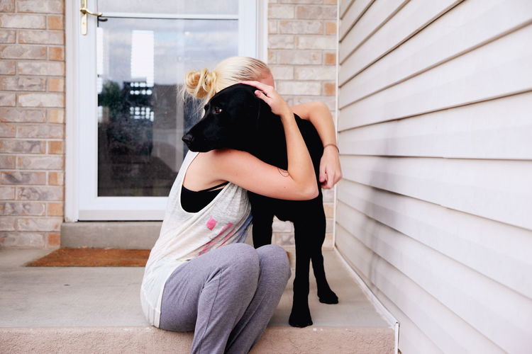 Woman embracing dog while sitting at porch
