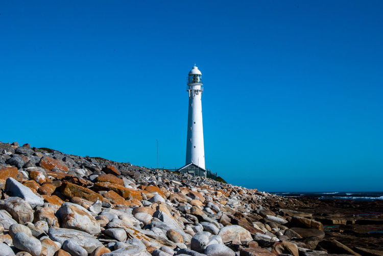 Lighthouse on rock against blue sky