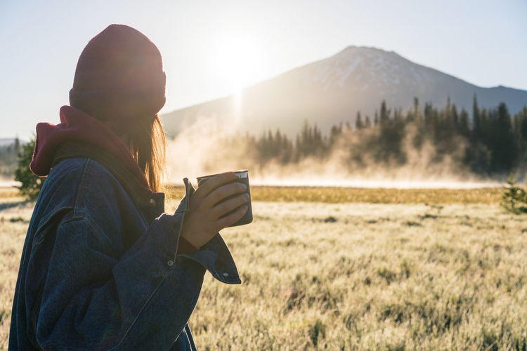 Young woman holding coffee at sunrise looking at foggy mountain