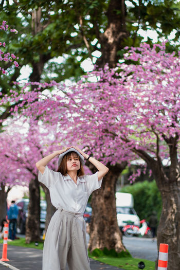 Full length of woman standing by pink flower tree