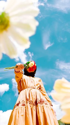 Low angle view of woman holding flower against sky