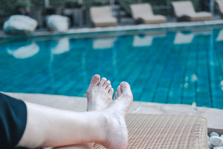 Low section of person relaxing at swimming pool
