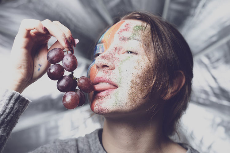 Woman with glittery face eating red grape at home