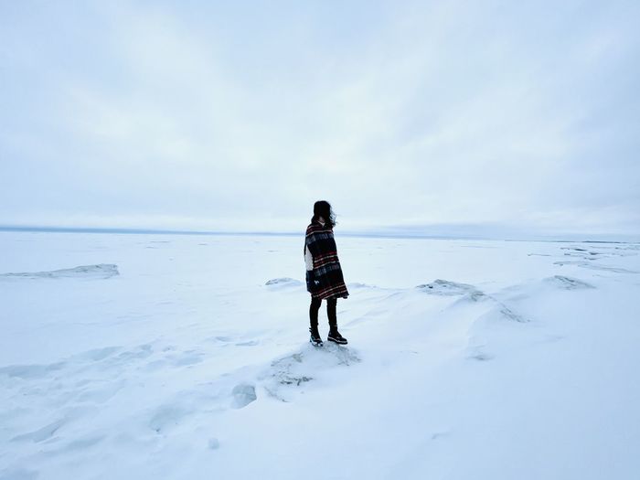 View of woman in the middle of a windy, vast snow covered lake against sky