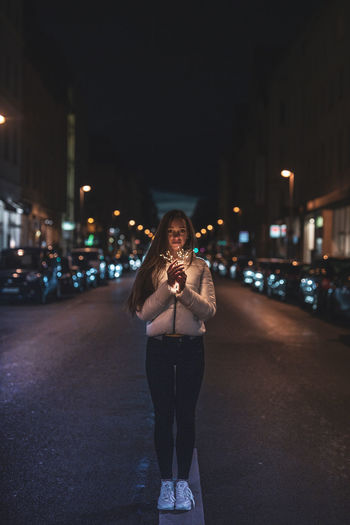 Portrait of young woman standing on illuminated street at night