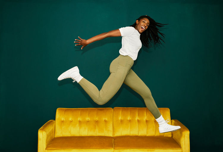 Side view of young woman jumping against gray background