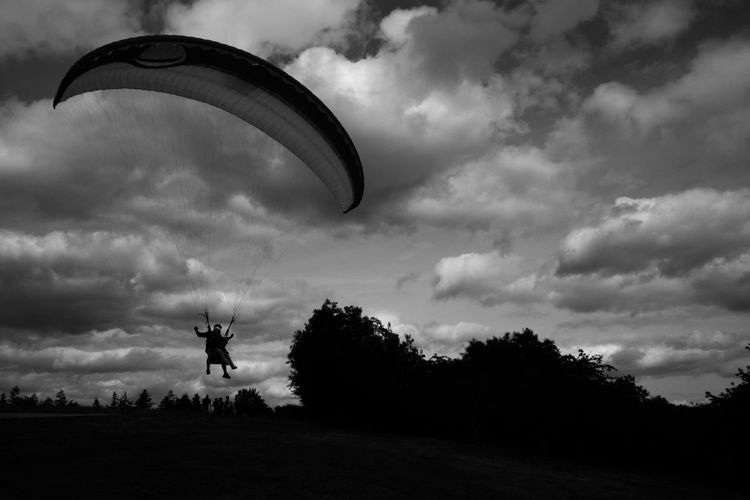 Silhouette person paragliding over field against sky