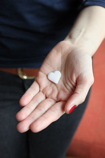 Midsection of woman holding heart shape pill