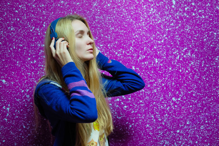 Woman listening music while standing against colored background