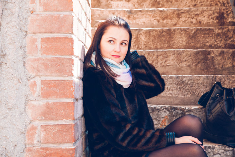 Portrait of teenage girl sitting against brick wall