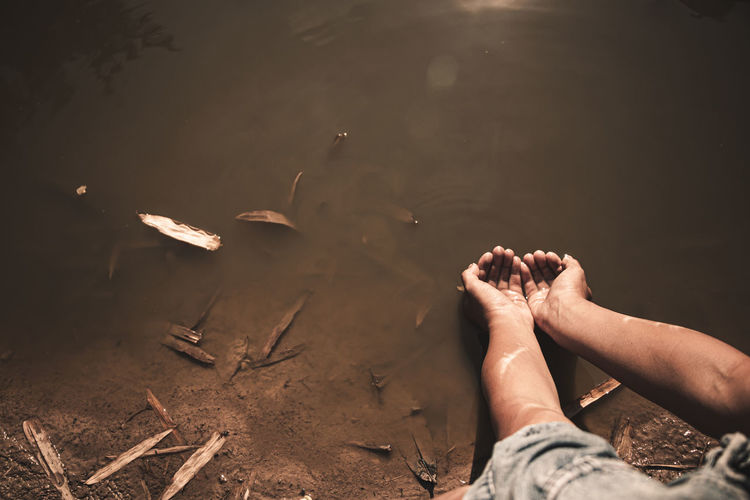Cropped image of hands holding water over lake