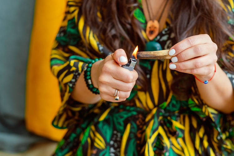 A stick of palo santo tree in the hands of a girl. a woman lights a stick. close up.