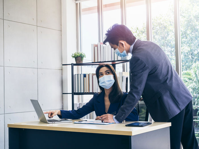 View of business people wearing flu mask brainstorming at office