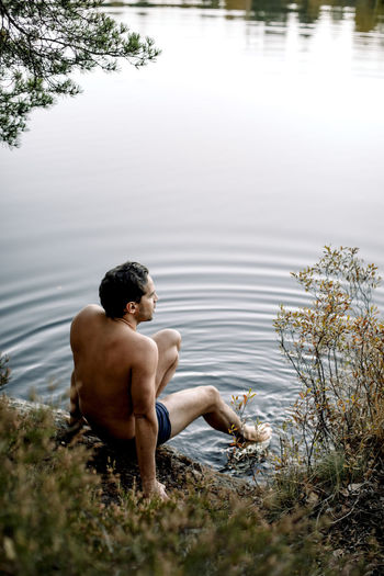 Shirtless man sitting near lake during staycation