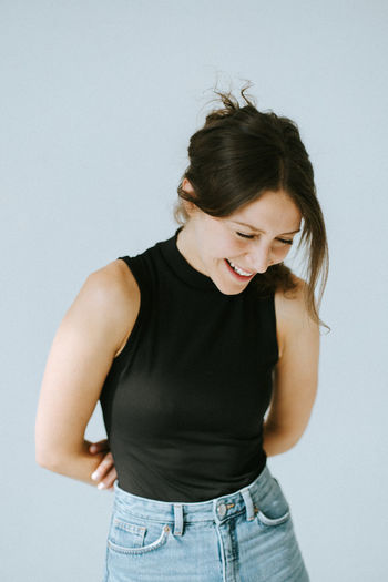 Young woman laughing while ooking away while standing against white background