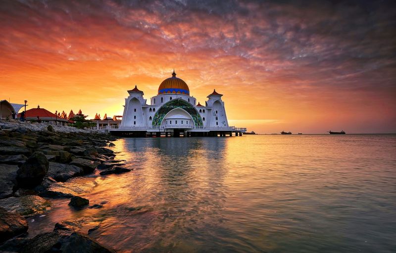 Malacca straits mosque by sea against orange sky during sunrise