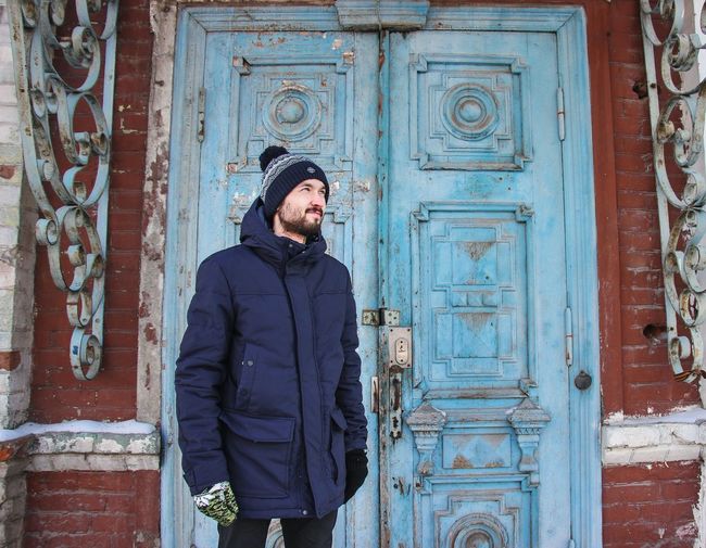 Man standing in warm clothing against closed blue door