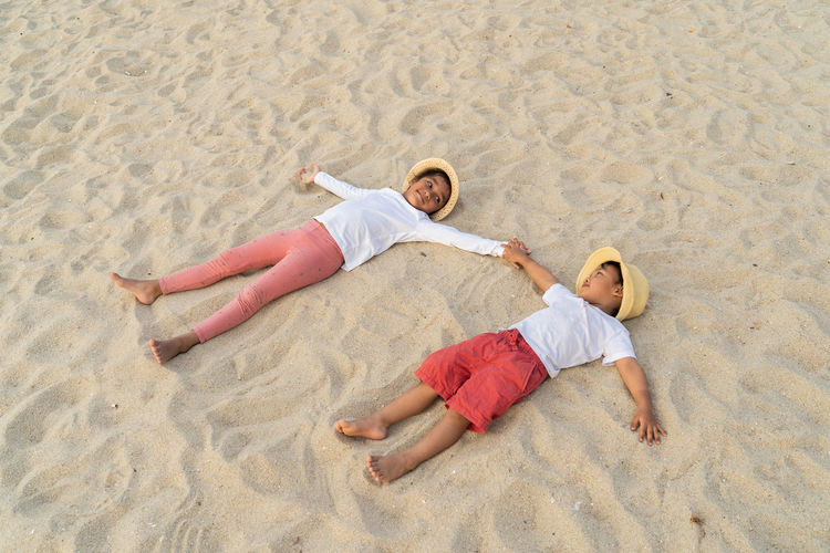 High angle view of siblings lying on sand at beach
