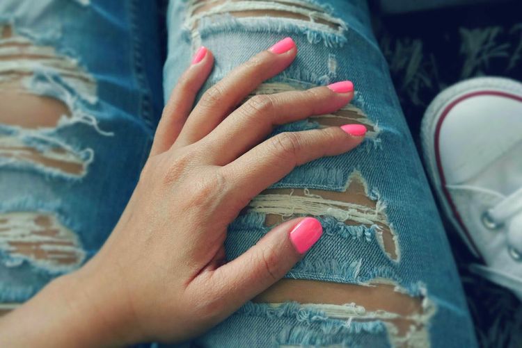 Close-up of hand touching ripped jeans