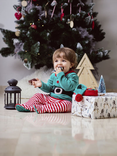 Full length of cute girl sitting on christmas tree
