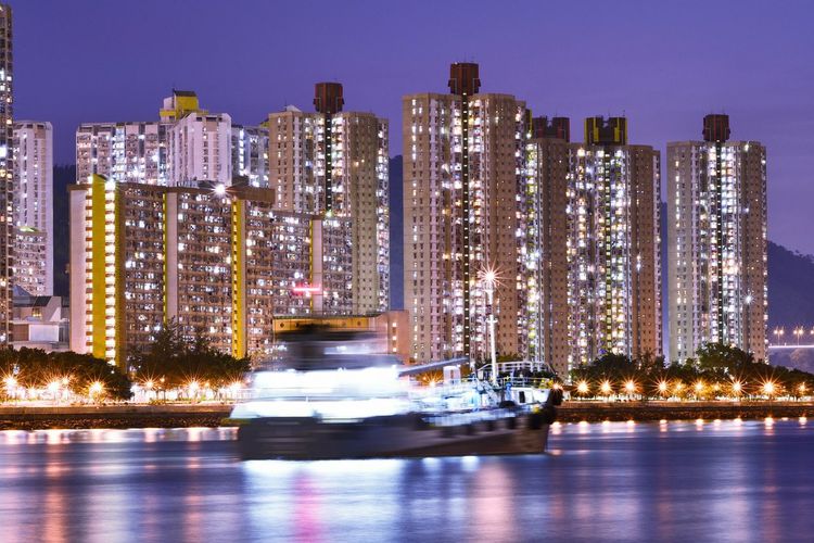 Blurred motion of boat sailing in river against illuminated buildings at night